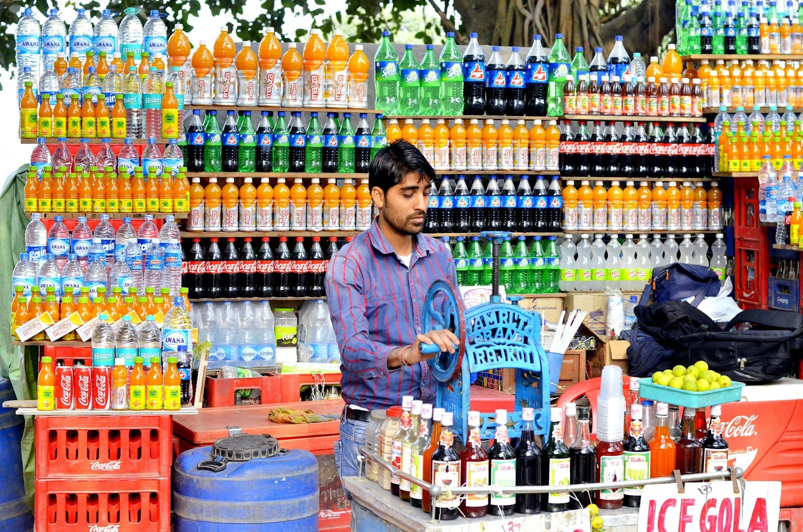A small Indian retailer standing behind a stall stacked with packaged drinks